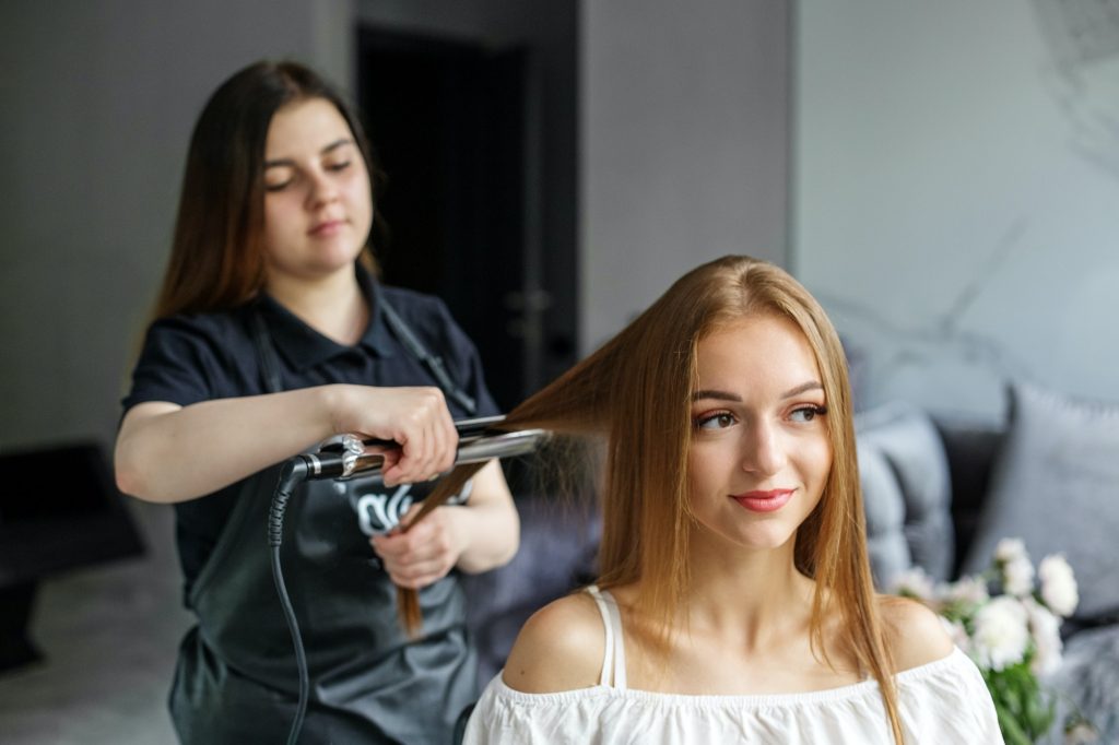 Hairdresser makes hair styling. Hair straightening with an iron. Young woman smiling. Good service